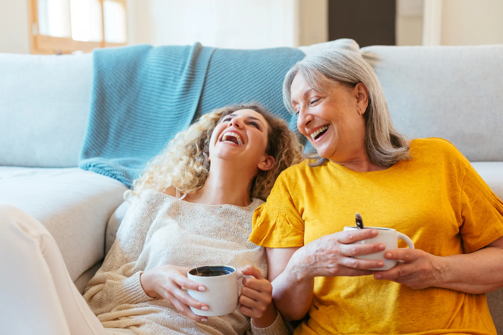mother and daughter smiling together holding a cup of tea.