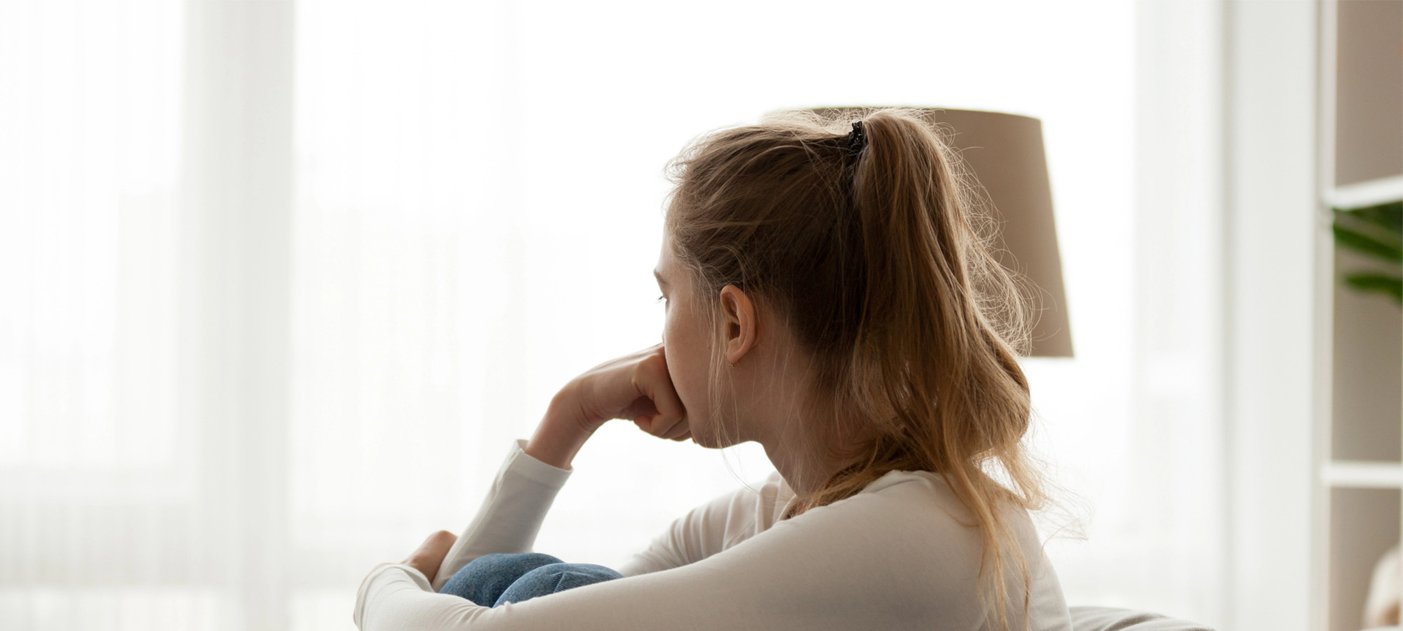 a distressed, isolated young person sits alone by a bright window, representing binge eating disorder shame.