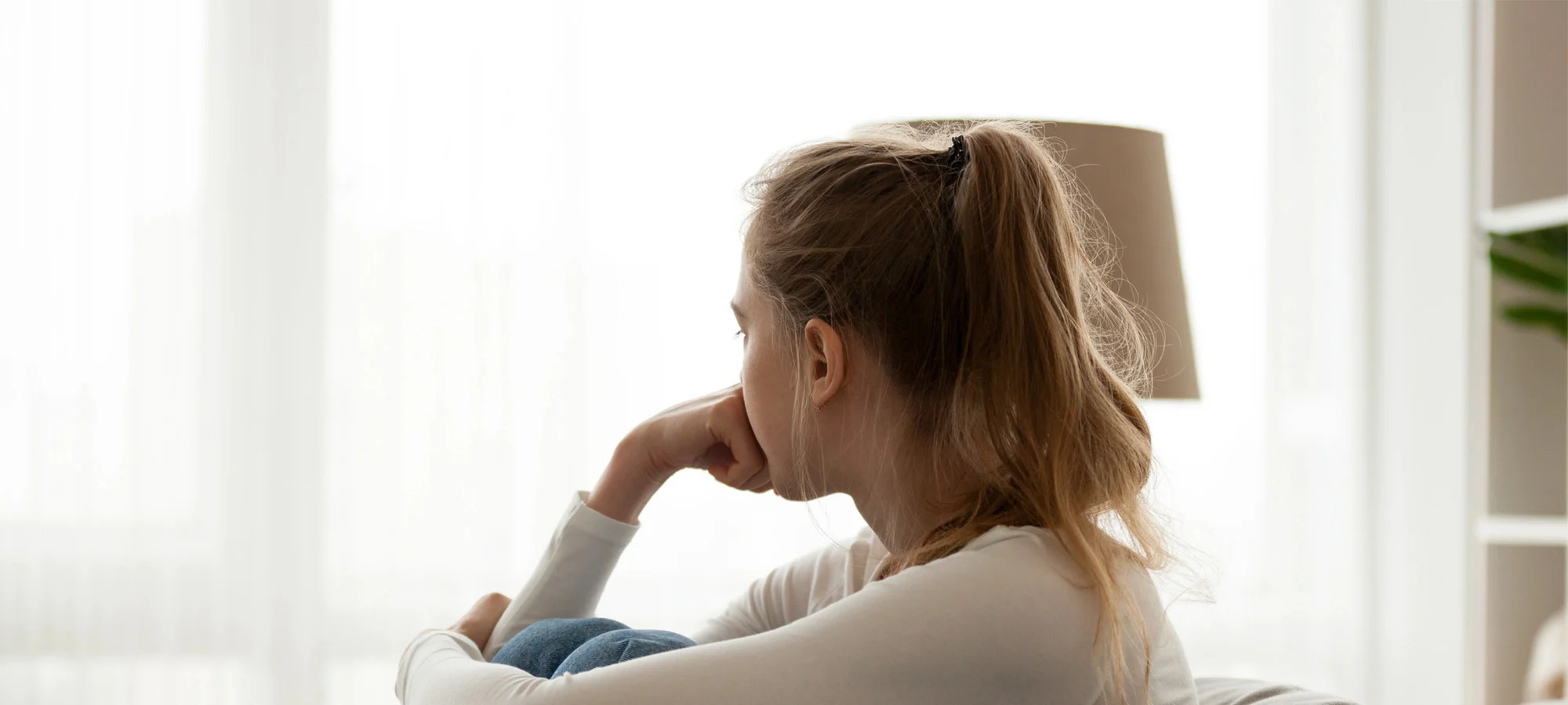 a distressed, isolated young person sits alone by a bright window, representing binge eating disorder shame.