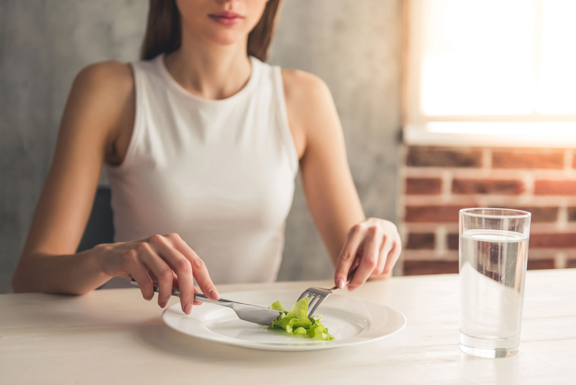 Person eating a small portion of lettuce, illustrating the primary distinction between bulimia nervosa and binge eating disorder