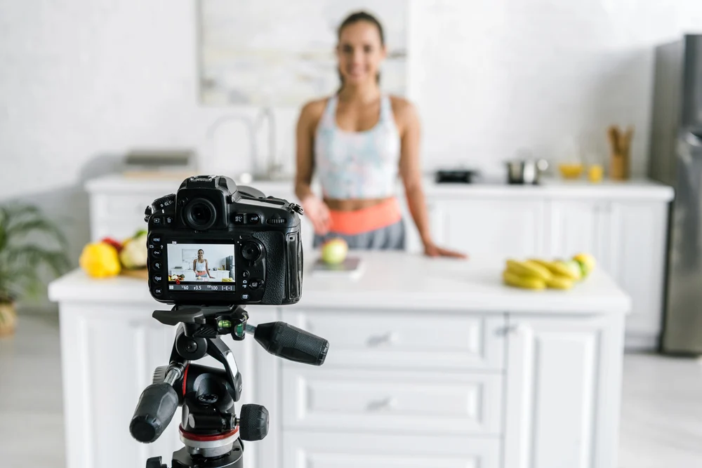 dslr camera on a tripod, recording a woman standing in a bright kitchen.