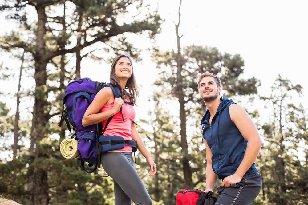 a smiling couple stops on a forest trail, and enjoying an outdoor adventure after significant weight loss.