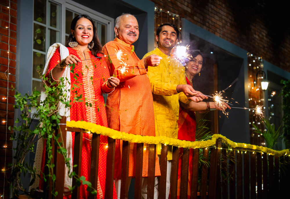The Ultimate Guide To Navigating Holidays With An Eating Disorder 1 a smiling family in traditional attire celebrates diwali on a decorated balcony, holding sparklers amid marigold garlands and string lights.