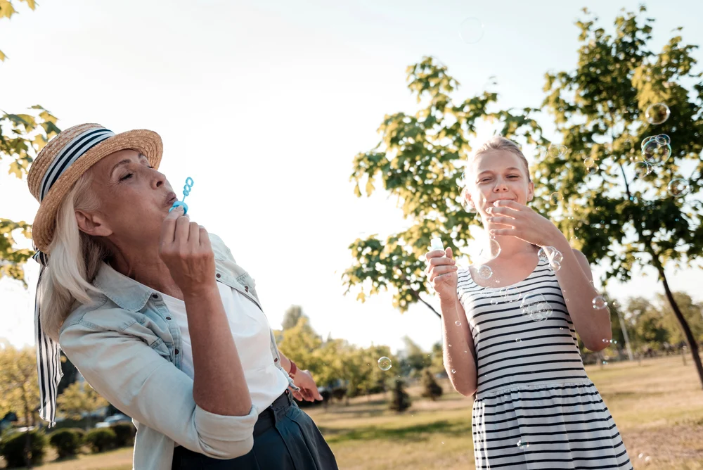 a mother and daughter enjoy a sunny park, smiling as they blow soap bubbles together.