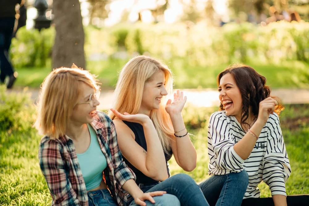 three young women sitting on the grass in a sunny park, representing hopeful recovery and social connection after orthorexia.